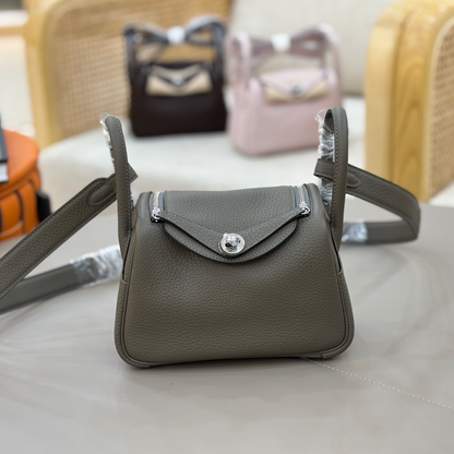 Muted Graphite Grey Pebbled Grain Compact Curved Saddle Shoulder Bag With Silvery Turn Lock Hardware, Dual Side Zip Closures And Base Defensive Round Studs
