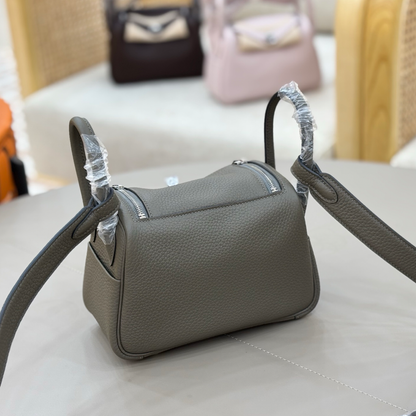 Muted Graphite Grey Pebbled Grain Compact Curved Saddle Shoulder Bag With Silvery Turn Lock Hardware, Dual Side Zip Closures And Base Defensive Round Studs